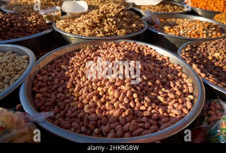 Close up of stainless steel scoop with roasted piled peanuts on display at street market. Peanuts in plastic bag ready for sale Stock Photo