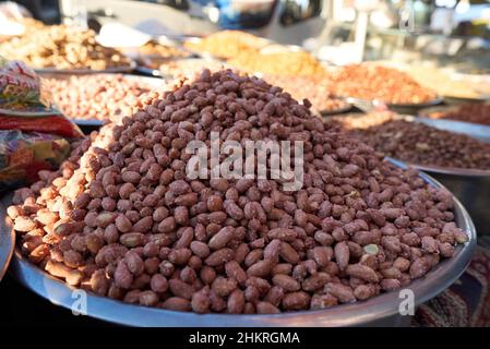 Close up of stainless steel scoop with roasted piled peanuts on display at street market. Peanuts in plastic bag ready for sale Stock Photo