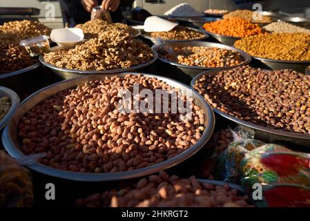 Close up of stainless steel scoop with roasted piled peanuts on display at street market. Peanuts in plastic bag ready for sale Stock Photo