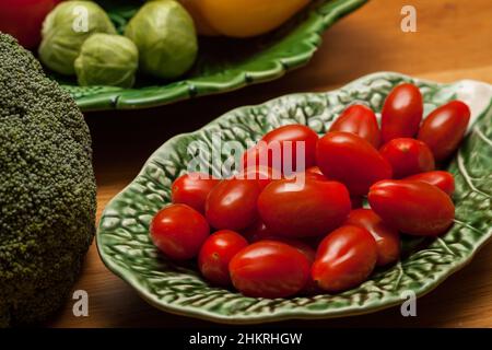 Vegetables, tomatoes, broccoli, brussels sprouts on green plates and wooden table Stock Photo