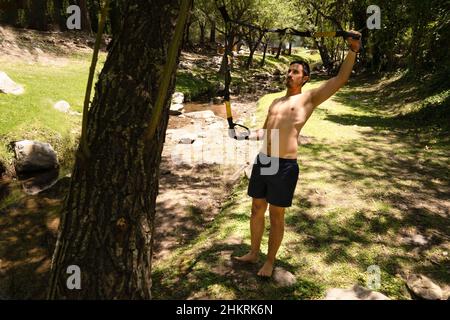 Handsome muscular man is training outdoor on TRX. Total Body Resistance Exercises. Stock Photo