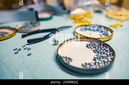 A lot of different metal bolts and nuts, plastic small components and professional tools lie on a blue desktop in a master worker's workshop under a c Stock Photo