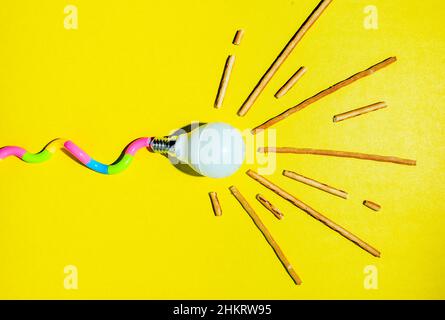 A creative composition of a light bulb and rays of light, a minimalistic concept, a stylized tadpole, on a yellow background. Stock Photo