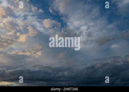 Aerial cloudscape of partly cloudy skies above, sun breaking through the clouds to the left and dark ominous storm front approaching below. Stock Photo
