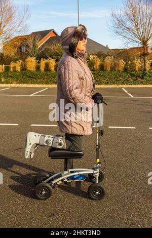 Knee scooter or walker being used by a woman with leg foot in surgical boot on sunny winter day, landscape, close up. Stock Photo