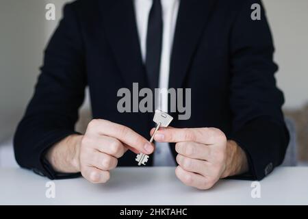 Young man in a suit holding a key from a new apartment in his hand. Realtor, home loan concept. Stock Photo