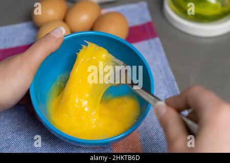 beating hen's eggs in a blue bowl with a fork Stock Photo