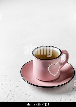 A pink cup with heart of tea standing on a plate on white textured background. Still life for St. Valentine's day Stock Photo