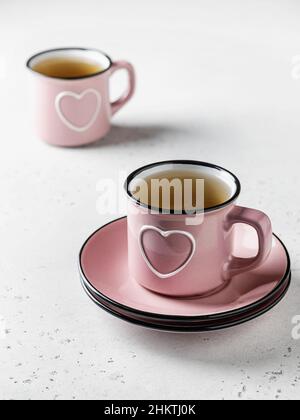 Two pink cups with hearts with tea standing on a white textured background. Drinking beverages together on St. Valentine's day Stock Photo