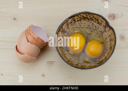 Cooking eggs in a coconut bowl. Protein ingredient for a healthy breakfast. Omelet preparation. Broken eggshells on the table. The transparent, yellow Stock Photo
