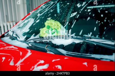 Bouquet of flowers in the car behind the windshield. Washing car. Driver's glass in foam. Stock Photo