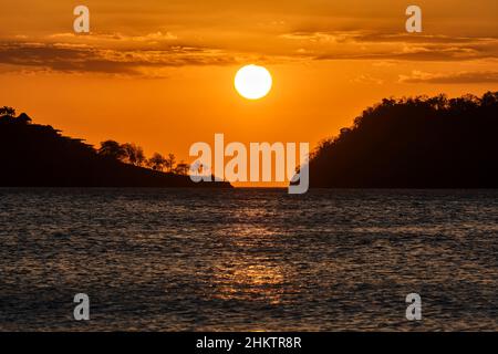 A beautiful image of the setting sun and hazy orange sky between two landmasses off the coast of Costa RIca. Stock Photo