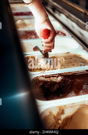 Close-up shot of a female hand scooping ice cream from a metal trays in the refrigerator at the shop Stock Photo