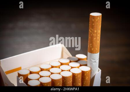 A macro photograph of the filter ends of an open pack of cigarettes. One cigarette sticks out. Stock Photo