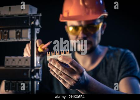 A male electrician works in a switchboard with an electrical connecting cable. Stock Photo