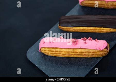 Chocolate and berry eclairs close-up on a black background. Stock Photo