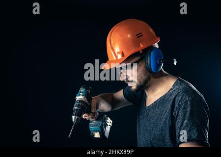 A young man in overalls protective helmet hard hat hold electric drill. Stock Photo
