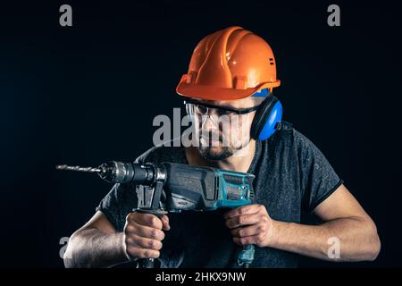 A young man in overalls protective helmet hard hat hold electric drill. Stock Photo