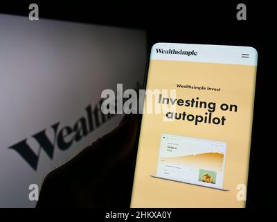 Person holding cellphone with website of Canadian financial services company Wealthsimple on screen with logo. Focus on center of phone display. Stock Photo
