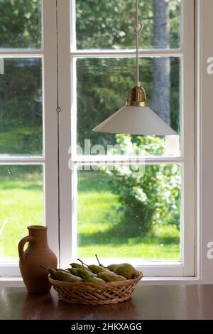 Still life of clay pot and pears in wicker basket on the wooden table near window Stock Photo