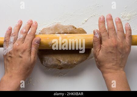 Woman hands rolling out gingerbread dough by rolling pin on the white background Stock Photo
