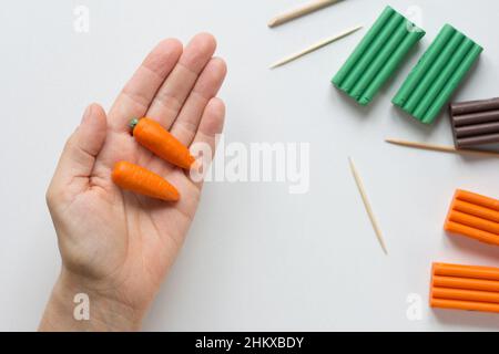 Two handmade small carrots made from polymer clay on woman hand on the white background Stock Photo