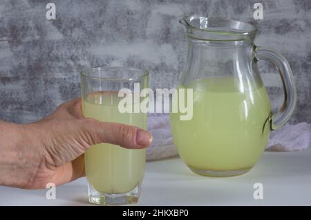 Liquid whey that remains after formation of curds in glass holding in woman hand on the white background Stock Photo