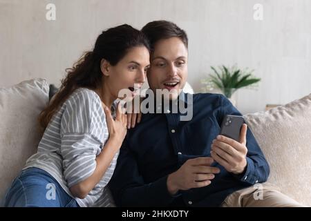 Surprised couple looking at smartphone screen, reading unexpected news Stock Photo