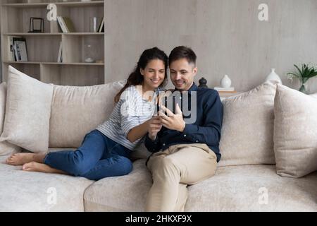 Happy couple using smartphone, relaxing on couch together Stock Photo