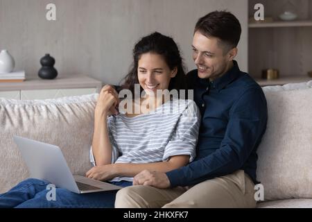 Happy couple using laptop together, relaxing on couch Stock Photo