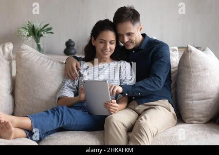 Smiling young couple using tablet together, sitting on couch Stock Photo