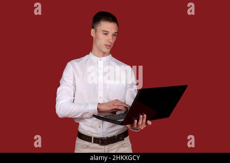 Holding laptop. Young Businessman using his laptop PC. Smiling handsome man working laptop. Happy young man using laptop computer on red background. Stock Photo