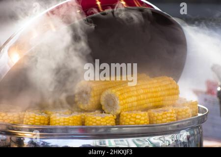 Boiled corn in a saucepan with hot water and steam on a city street, selling boiled corn Stock Photo