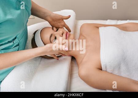 Pretty woman getting facial and head massage at wellness spa. Face massage with perfect clean and fresh skin, close-up Stock Photo