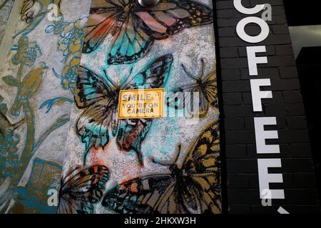 Smile you're on camera security sign on a butterfly decorated building wall in Brisbane Australia Stock Photo