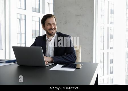 Happy dreamy business professional man working at laptop in office Stock Photo