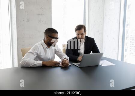 Focused diverse businessmen in formalwear using laptop at office table Stock Photo