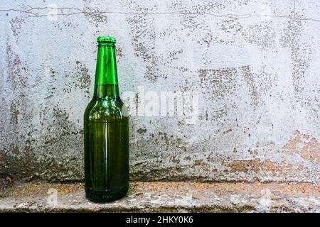 A bottle with an alcoholic drink stands against an old concrete wall Stock Photo