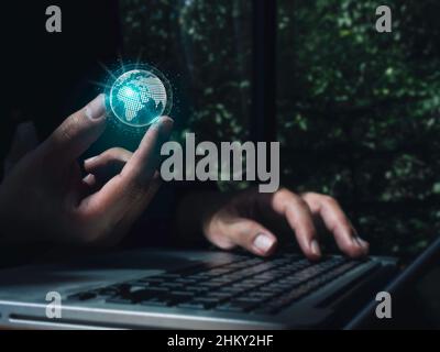 Hand holding a futuristic virtual small blue planet, digital link tech while using a laptop computer on dark. Future global network connection and big Stock Photo