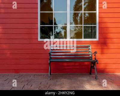 Empty black wrought iron bench decorated in front of the red wood plank building near the white window glass. Stock Photo