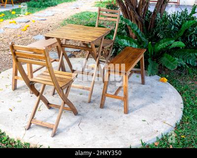 Outdoor garden table set. Empty wooden table with two chairs and two benches on round concrete floor on green grass near the walkway in the park, nobo Stock Photo