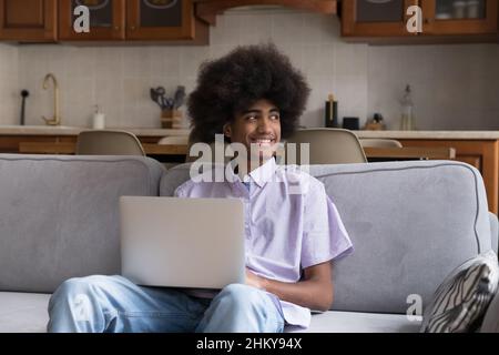 Happy thoughtful Black student guy with Afro hairdo using laptop, Stock Photo