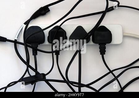 Four plugs connected to a multi socket extension lead with the cables forming an untidy mess. Stock Photo