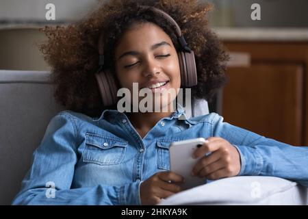 Smiling gen Z teen Black girl wearing big wireless headphones Stock Photo