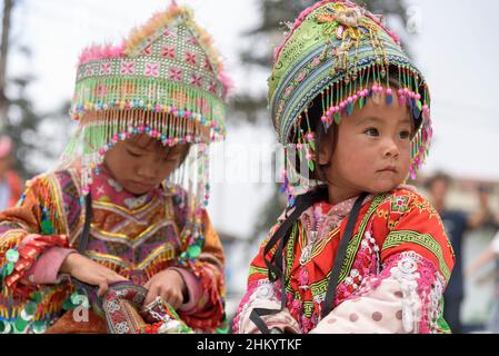 Young girls, wearing traditional Hmong tribe clothing, wait to pose for photographs by tourists in the town square, Sapa (Sa Pa), Lao Cai, Vietnam Stock Photo