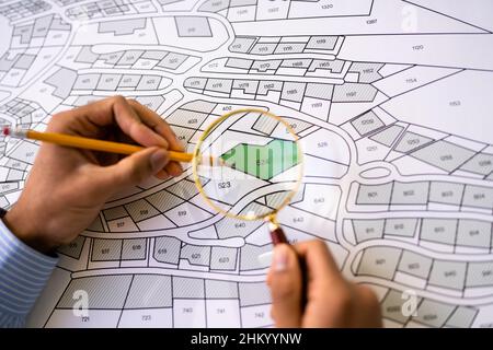 Close-up Of Human Hand Holding Pencil Over Paper Cadastre Map Stock Photo