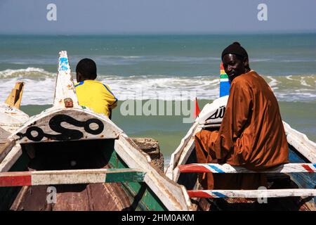 Portrait of Sahelian fishermen sitting in their brightly painted pirogues in Saint-Louis, Senegal, looking at the camera and the Atlantic Ocean Stock Photo