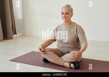 Contemporary senior female in activewear sitting in lotus position on mat while practicing relaxation yoga exercises at leisure Stock Photo