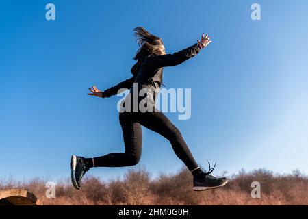 young female runner is jumping over wooden hurdles in countryside - concept of health and wellness Stock Photo