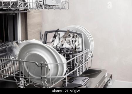 Front view of open automatic stainless steel built-in fully integrated top control dishwasher range machine with clean utensils, cutlery, glasses, dishes, plates inside in modern home kitchen Stock Photo
